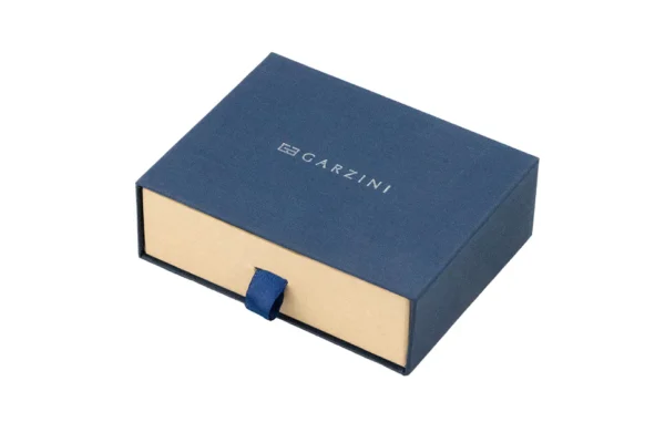 A embalagem premium de cartão protege a Carteira Garzini MagSafe Metal Wallet Azul Escuro no seu interior. Além disso, a caixa de oferta apresenta uma janela transparente que deixa ver a Carteira Garzini MagSafe Metal Wallet Azul Escuro com total clareza antes da abertura