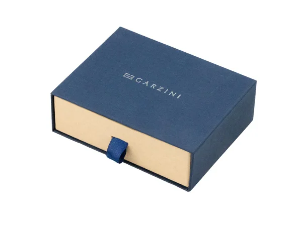 A embalagem premium de cartão protege a Carteira Garzini MagSafe Metal Wallet Azul Escuro no seu interior. Além disso, a caixa de oferta apresenta uma janela transparente que deixa ver a Carteira Garzini MagSafe Metal Wallet Azul Escuro com total clareza antes da abertura