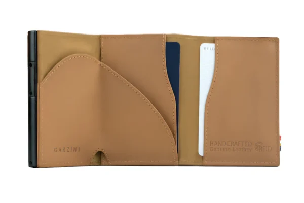 A Carteira Garzini MagSafe Metal Wallet Azul Camel surge aberta mostrando o seu interior tecnológico. Além disso, a Carteira Garzini MagSafe Metal Wallet Azul Camel destaca-se pela sua elegante textura de couro legítimo castanho.