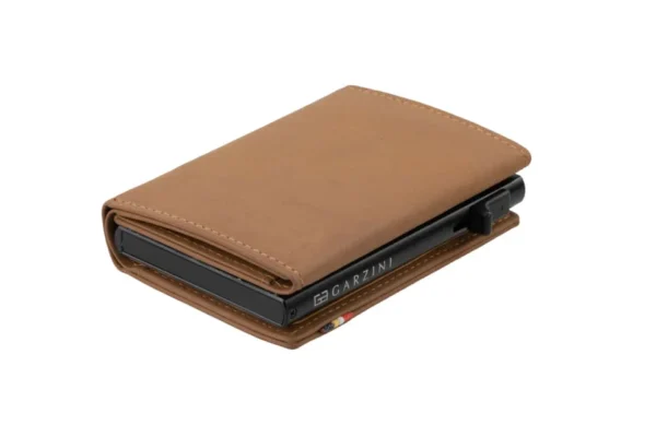 A Carteira Garzini MagSafe Metal Wallet Azul Camel surge aberta sobre um fundo branco. Além disso, a Carteira Garzini MagSafe Metal Wallet Azul Camel destaca-se pela sua elegante textura de couro legítimo castanho claro.