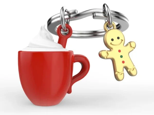 O Porta-chaves Chocolate Quente com Caneca e Biscoito Metalmorphose exibe uma chávena vermelha cheia de natas ao lado de um boneco de gengibre. Além disso, o Porta-chaves Chocolate Quente com Caneca e Biscoito Metalmorphose destaca-se pelos seus reflexos brilhantes sobre o fundo branco.