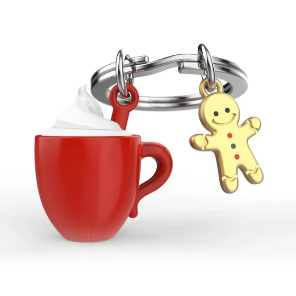 O Porta-chaves Chocolate Quente com Caneca e Biscoito Metalmorphose exibe uma chávena vermelha cheia de natas ao lado de um boneco de gengibre. Além disso, o Porta-chaves Chocolate Quente com Caneca e Biscoito Metalmorphose destaca-se pelos seus reflexos brilhantes sobre o fundo branco.